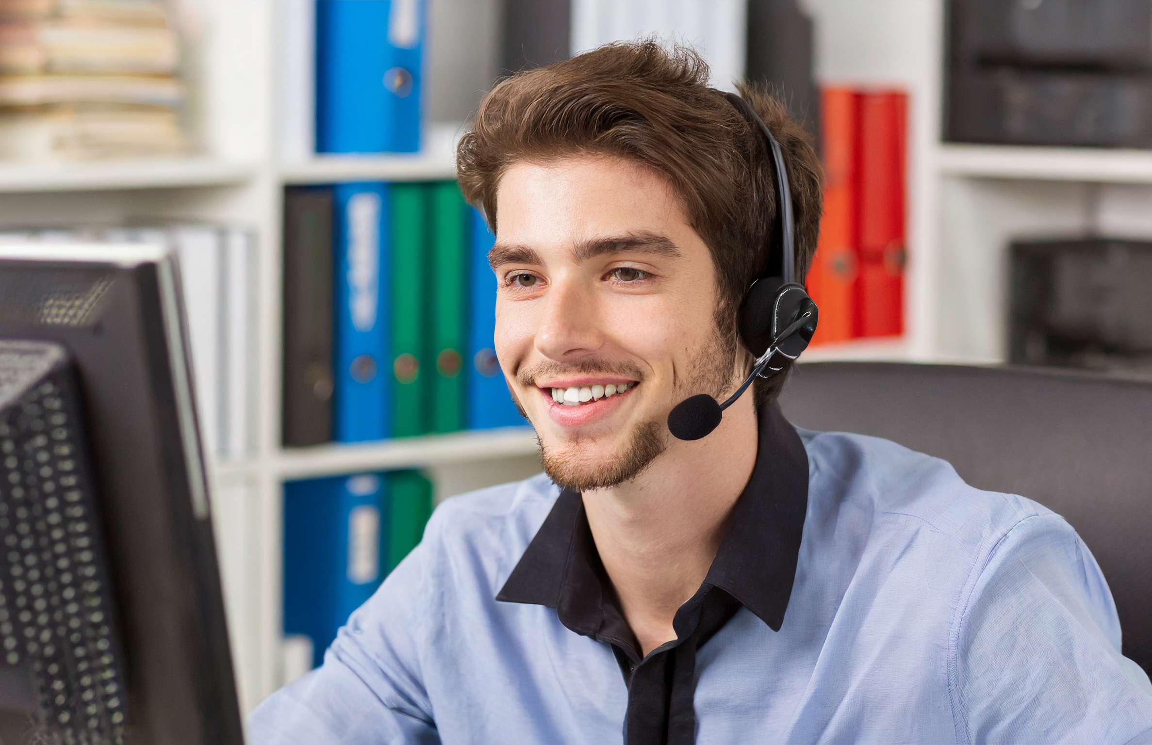Lächelnder junger Mann telefoniert mit einem Headset mit Kunden